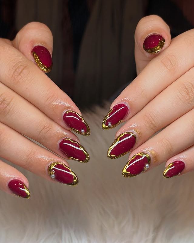 Burgundy almond nails with gold chrome edges and pearls